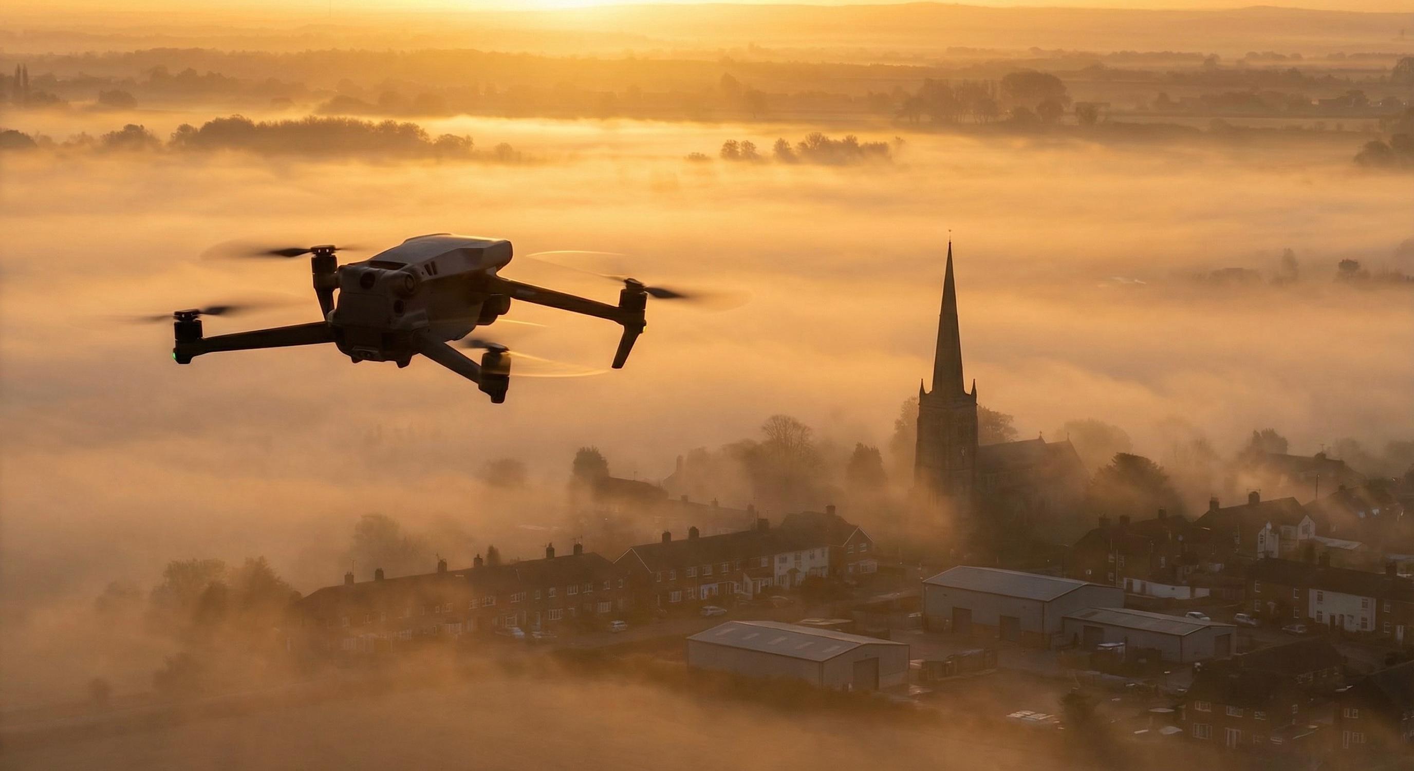 Professional drone flying above misty English village at golden sunrise, Northamptonshire