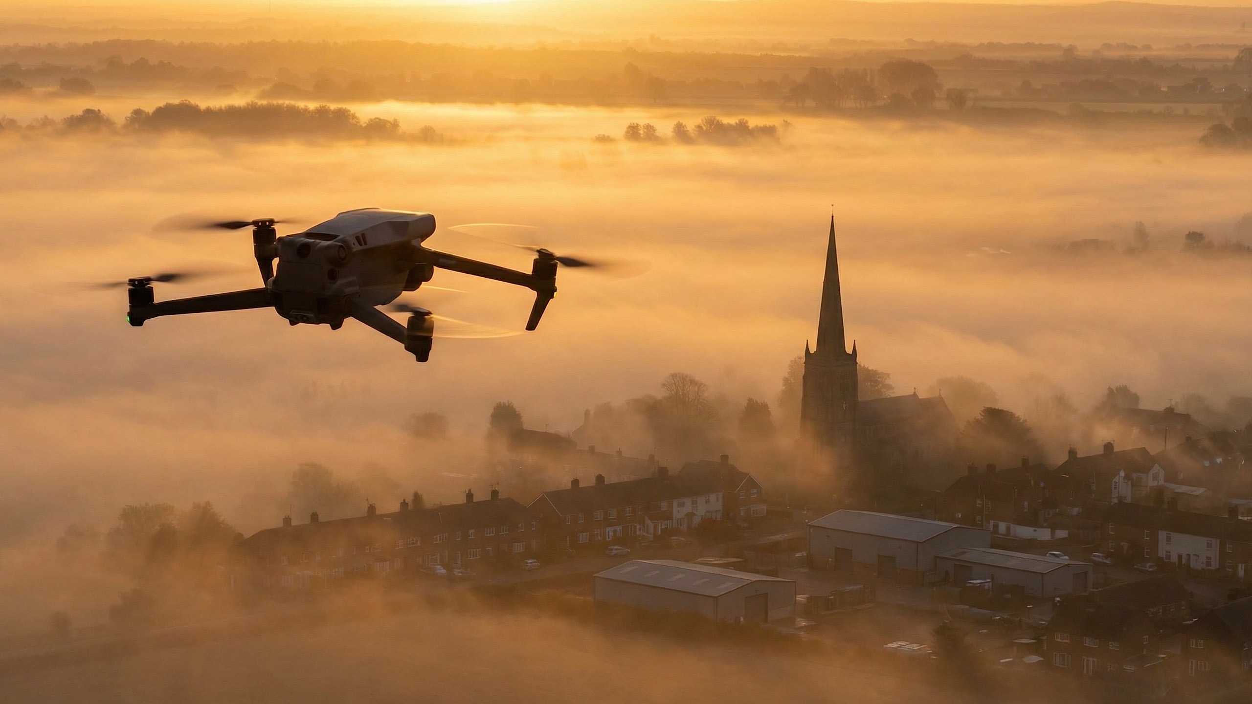 Professional drone flying above misty English village at golden sunrise, Northamptonshire