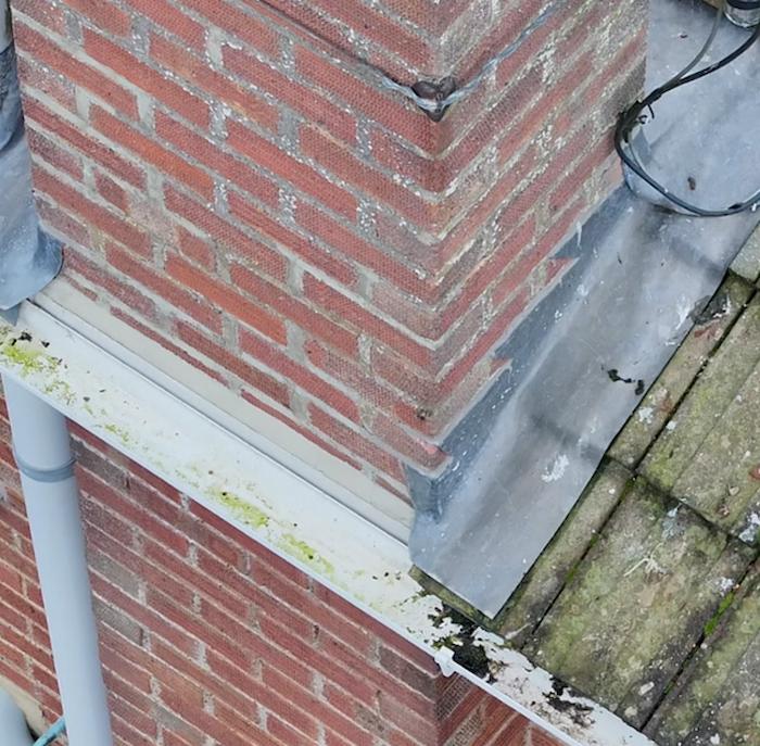 Close-up RGB aerial view of chimney flashing junction showing algae staining and debris